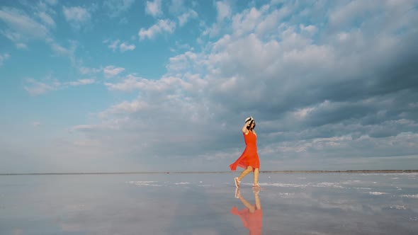 Portrait of a Young Woman in a Fluttering Dress. Girl Traveler Walks on a Pink Salt Lake alt