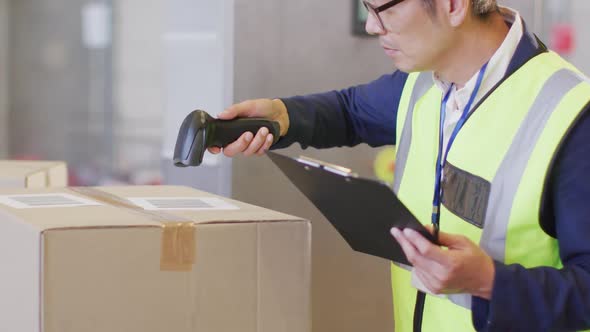Asian male worker wearing safety suit and scanning boxes in warehouse alt