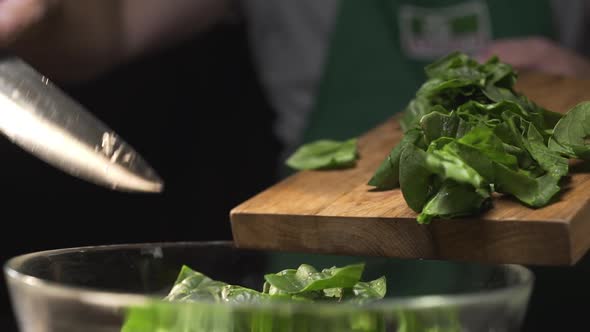The Cook Pours Chopped Spinach From the Cutting Wooden Board To the Glass Bowl alt