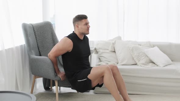 Sportive Young Man Is Doing Triceps Exercise Near Armchair at Home, Side View