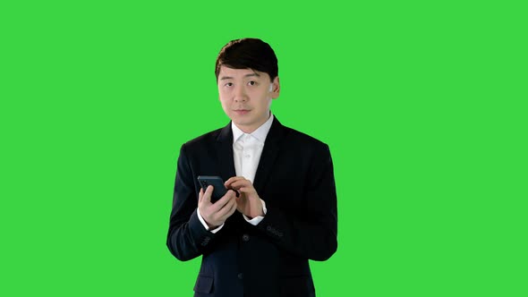 Asian Man in Suit Walks Using Mobile Phone on a Green Screen Chroma Key