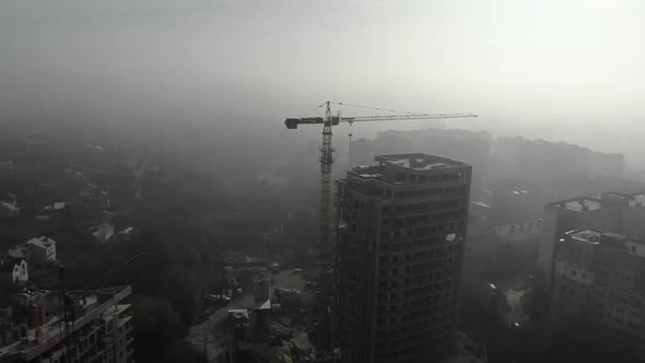 Birds eye view on tower crane in fog standing next to residential building. alt
