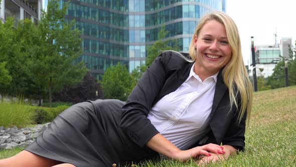 A Young Beautiful Businesswoman Lies in Grass in a Park and Sticks Her Tongue Out at the Camera alt