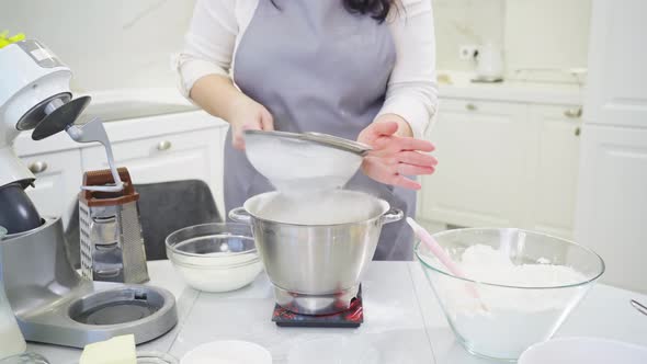 Cook Sifts the Flour Through a Sieve to Prepare Dough in a Mixer Bowl on Scale alt