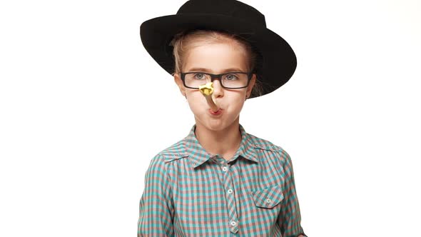 Small Beautiful Caucasian Kid Girl in Plaid Shirt Black Hat and Glasses Blowing Party Whistle on alt