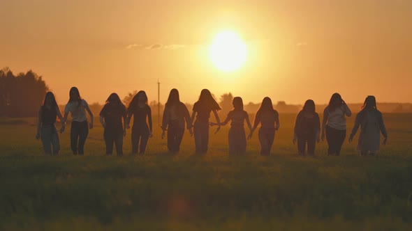 A Silhouette of 11 Girls Friends Waving Their Hands at Sunset in a Field and Then Running Away alt