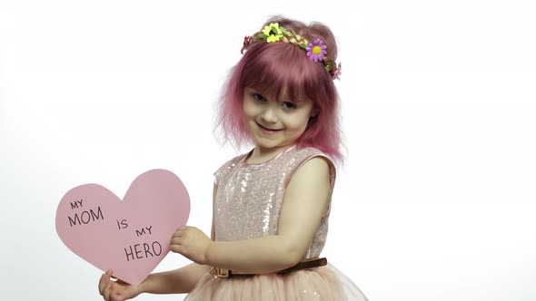 Child Girl Princess Holds Pink Paper Heart with Text About Mother. Mother's Day alt