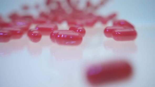 Red Shining Capsules Rolling Into The Camera On White Background