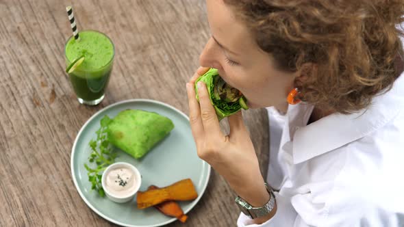 Top View of Young White Woman Takes a Bite of Her Delicious Vegan Burrito Served with Sauce a Side alt
