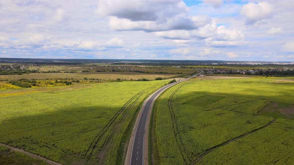 Aerial View of Intercity Road Between Green Agricultural Fields with Fast Driving Cars alt