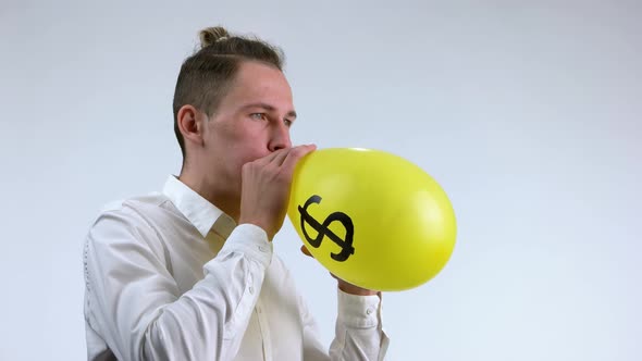 Young Man Blowing Dollar Balloon with Air. alt