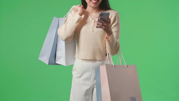 Woman Holding Shopping Bags Use Mobile Phone And Smile While Walking In Front Of Green Screen alt