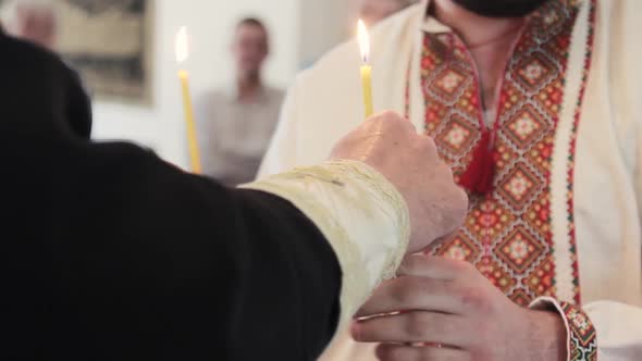 Man holds two candles in a temple in a traditional Ukrainian dress at christening. Hands close up