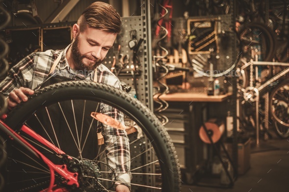 Stylish bicycle mechanic doing his professional work in workshop.