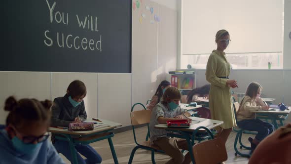 Multi Ethnic Students in Face Masks Doing Test in Classroom with Teacher alt