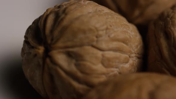Cinematic, rotating shot of walnuts in their shells on a white surface alt