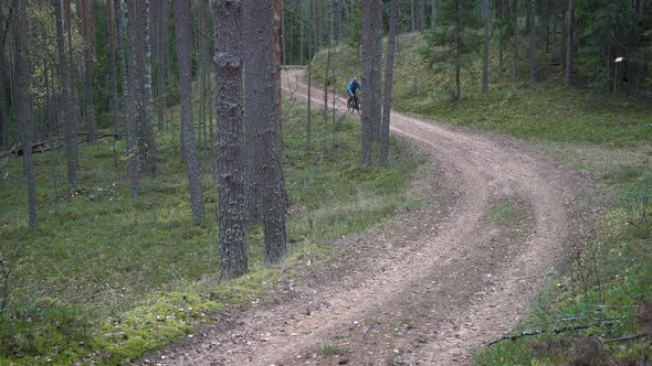 Man Biker is Riding Bicycle Along Rural Ground Road in Forest Back View