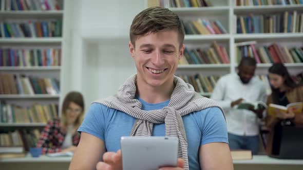 Guy Sitting in the University Library and Using i-pad for Searching Needed Information for Home Task alt