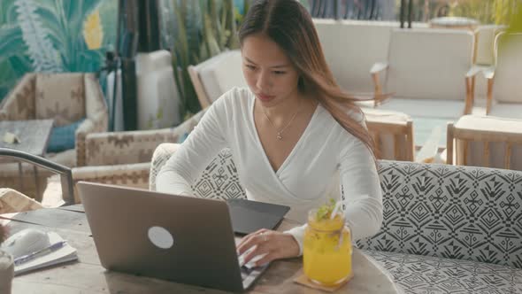 A Young Asian Girl Works at Her Laptop in a Rooftop Cafe in the City alt