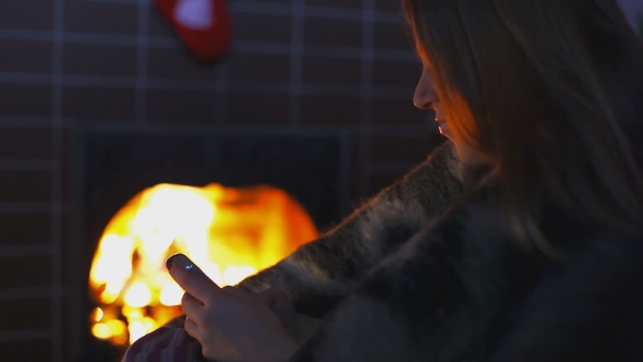 Girl Near The Fireplace With Her Smartphone
