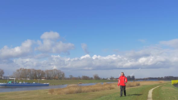 Backpacker is Walking Along a River Toward Camera alt