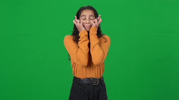 Excited Teen African American Girl Crossing Fingers Closing Eyes Standing at Chromakey Background alt