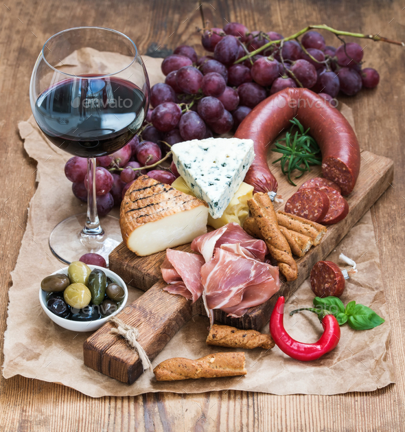 Glass of red wine, cheese and meat board, grapes,fig, strawberries, honey, bread sticks