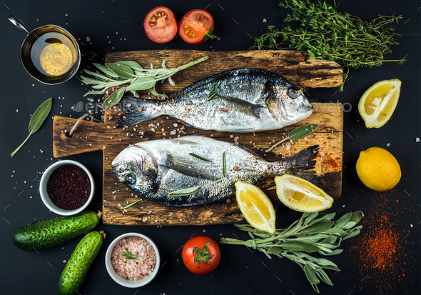 Fresh uncooked dorado or sea bream fish with lemon, herbs, oil, vegetables and spices - Stock Photo - Images