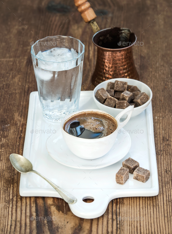Cup of black coffee, copper pot, water with ice in glass and cane sugar cubes
