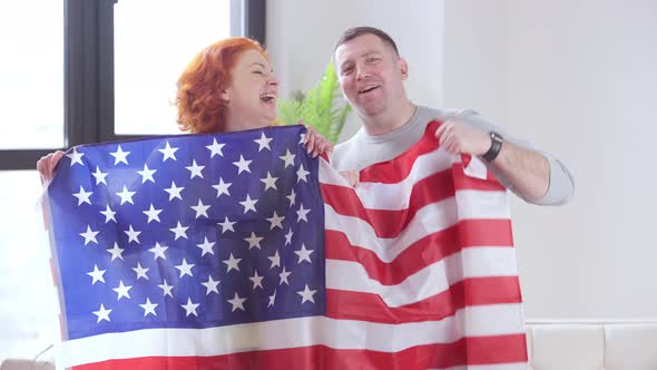 Proud Adult Couple Posing with American Flag Showing Thumb Up and Looking at Camera with Toothy alt