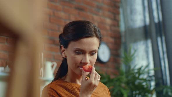 Woman Tasting Tomato in Kitchen. Young Girl Eating Piece of Tomato at Home alt