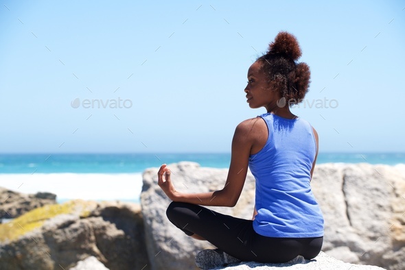 Young african woman sitting at beach in yoga pose - Stock Photo - Images