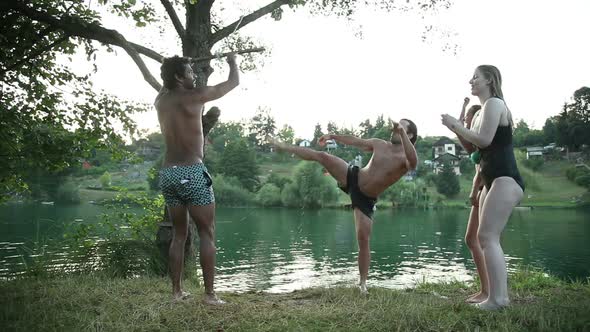 Young Man Having Fun With Friends Jumping Off Rope Swing Into River alt