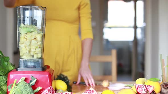 Woman Pouring Water In Blender With Pineapple And Avocado alt