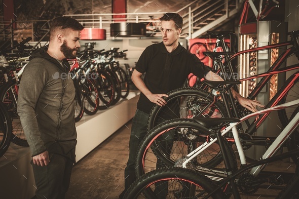 Salesman showing a new bicycle to interested customer in bike shop.