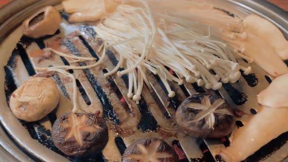 The Cook Prepares Mushrooms on Korean BBQ Gril Plate alt