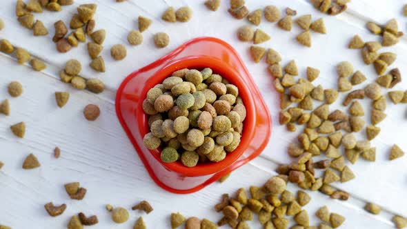 Top View of Dry Pet Food in a Red Bowl Rotating on a Wooden Table alt