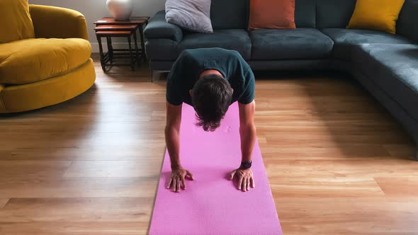 Young male performing Plank to Downward Dog yoga pose at home on yoga mat
