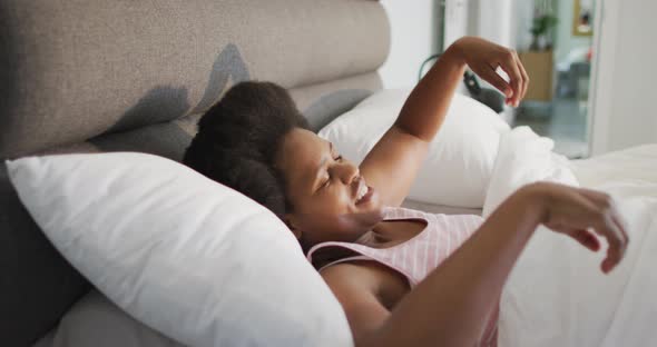 Happy african american woman lying in bed, stretching in bedroom alt