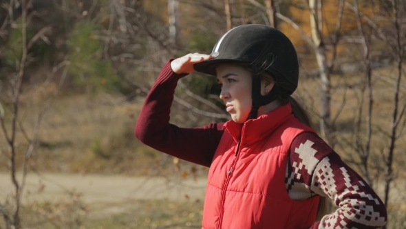 Woman Jockey Standing And Looking Into Distance Keeping Hand As a Visor alt
