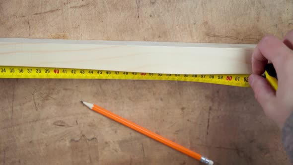 Hand Measures the Length of a Wooden Block with a Tape Measure Closeup alt