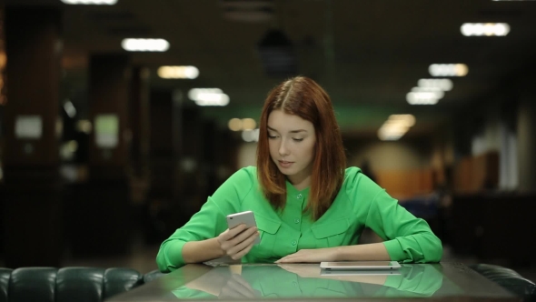 The Beautiful Woman Is Waiting For The Order Working With The Cellphone In Her Hands And Smiling. alt