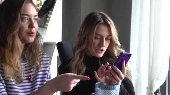 Two Female Friends Sitting in Cafe and Viewing Photos on Mobile Phone