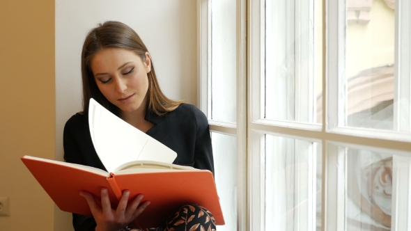 Beautiful Dreamy Young Lady Posing On The Windowsill And Reading a Book 