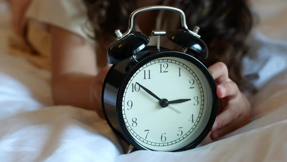 Child sets the ring time on a black classic alarm clock alt