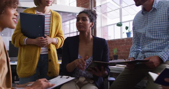 Mixed race businesswoman using tablet in office discussing with diverse colleagues alt
