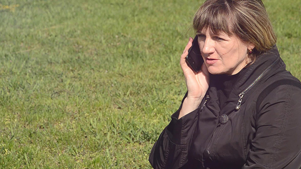 Woman Talking on Phone Sitting on a Green Meadow