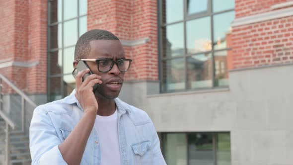 African Man Getting Angry on Call While Walking in Street Side View alt