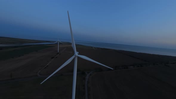 FPV Flight Over Wind Farms in the Field at Evening