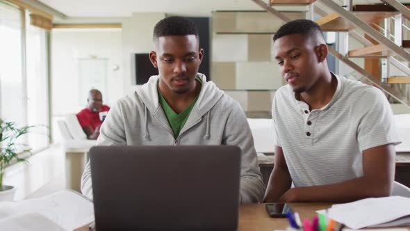 Two african american teenage twin brothers using a laptop and talking with father in background alt